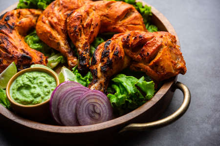Tandoori chicken is a chicken dish prepared by roasting chicken marinated in yogurt and spices in a tandoor or a clay oven, served with onion and green chutneyの写真素材