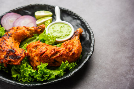 Tandoori chicken is a chicken dish prepared by roasting chicken marinated in yogurt and spices in a tandoor or a clay oven, served with onion and green chutneyの写真素材