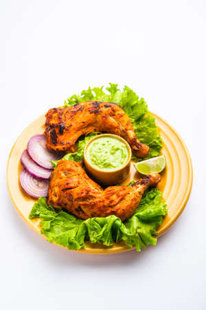 Tandoori chicken is a chicken dish prepared by roasting chicken marinated in yogurt and spices in a tandoor or a clay oven, served with onion and green chutneyの写真素材