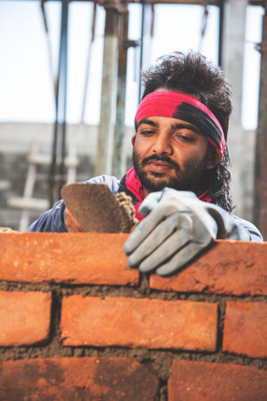 Happy Indian male construction worker constructing brick wall - hard working concept, manual labourの写真素材