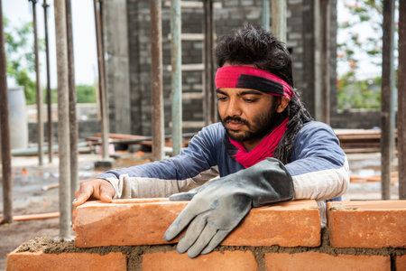 Happy Indian male construction worker constructing brick wall - hard working concept, manual labourの写真素材