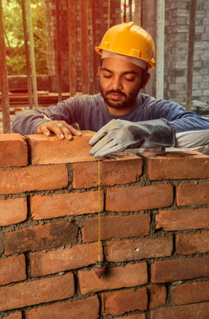 Happy Indian male construction worker constructing brick wall - hard working concept, manual labourの写真素材