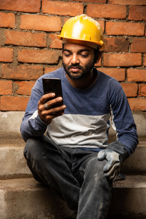 Happy smiling young indian construction labour busy on mobile phone at workplaceの写真素材