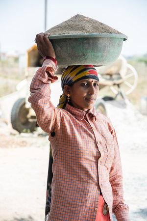 Asian Indian woman labour or coolie working at construction site Carrying sand on her head.の写真素材