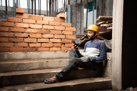Happy smiling young indian construction labour busy on mobile phone at workplaceの写真素材