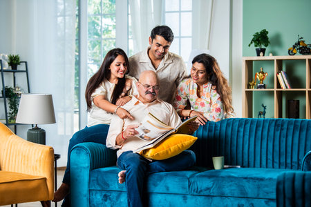 Indian family looking at Photo album while sitting on sofa, happy momentの写真素材