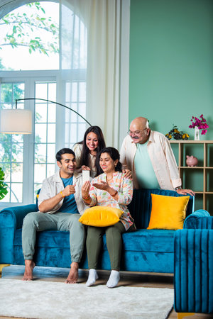 Cheerful Indian family having fun while using smartphone at homeの写真素材