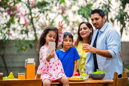 indian young family of four eating meal on dining table in the garden