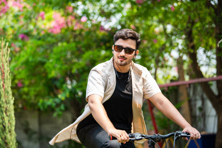 Asian indian young man using smartphone while riding on bicycleの写真素材