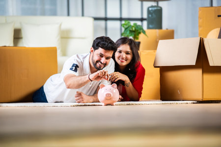 Indian couple saving money in piggybank while sitting in their new homeの写真素材