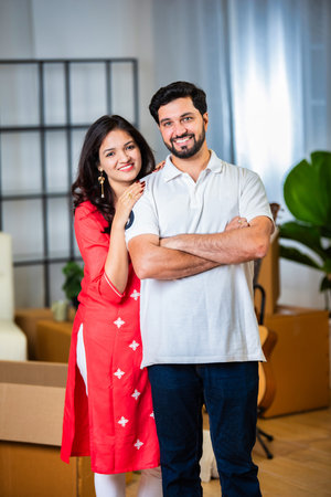 Indian young couple standing together in new house and looking at camera with smileの写真素材