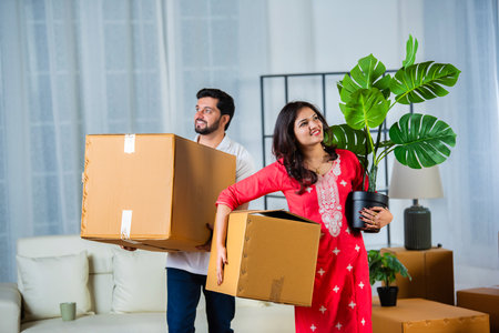 Indian young couple shifting home holding boxes in new homeの写真素材