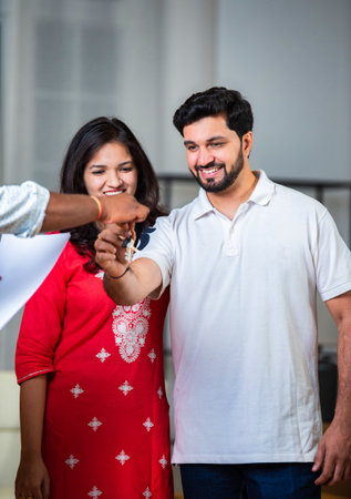Happy Indian young couple taking keys of their new house from broker and smilingの写真素材