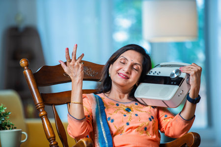 Retired asian Indian woman listen to old songs on vintage radio at home