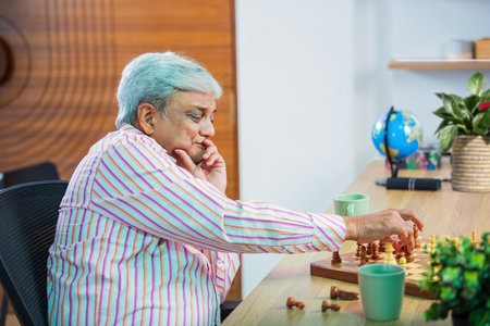 Senior Indian asian couple playing chess together at home on tableの写真素材