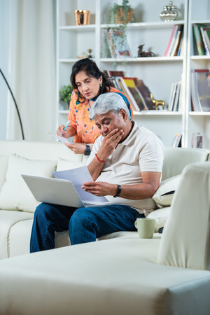 Retired Indian asian couple do paperwork at home with laptop, documents on sofa at homeの写真素材