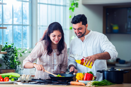 Happy loving Indian asian young couple cooking food in kitchen together, hugging, standing at table