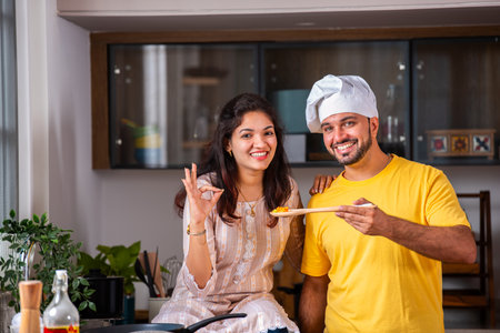 Happy loving Indian asian young couple cooking food in kitchen together, hugging, standing at tableの写真素材