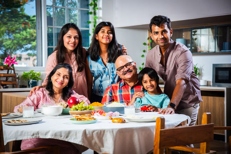 Portrait of Indian family of three generations eating meals together at home looking at camera