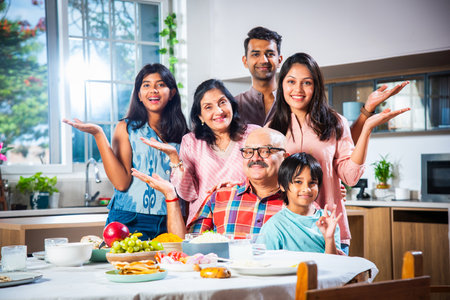 Portrait of Indian family of three generations eating meals together at home looking at camera