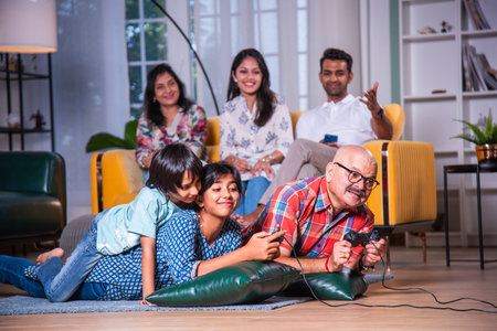 Indian asian grandpa playing video game with grandchildren lying on floor at home