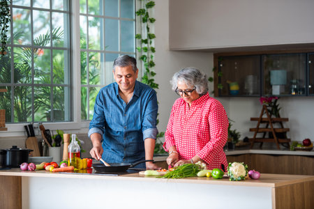 Senior Indian asian couple, cooking and having fun while preparing a healthy food in the kitchen at...