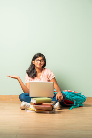 Indian asian school girl in casual wear using laptop for study sitting on floor isolatedの写真素材