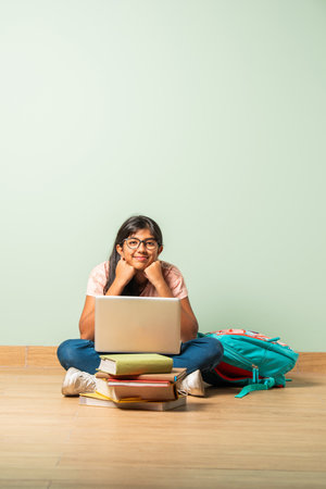 Indian asian school girl in casual wear using laptop for study sitting on floor isolatedの写真素材
