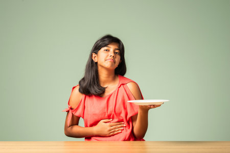 Sad or unhappy indian asian girl child saying no to food concept holding empty plateの写真素材