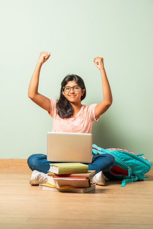 Indian asian school girl in casual wear using laptop for study sitting on floor isolated