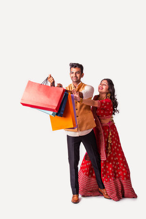 Indian asian couple with shopping bags in ethnic wear, standing isolated over white background. Diwali or festival saleの写真素材