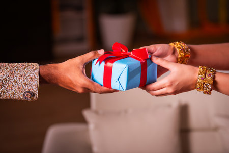 closeup of hands of Indian asian woman wears gold bangles in festival receiving gift box from manの写真素材