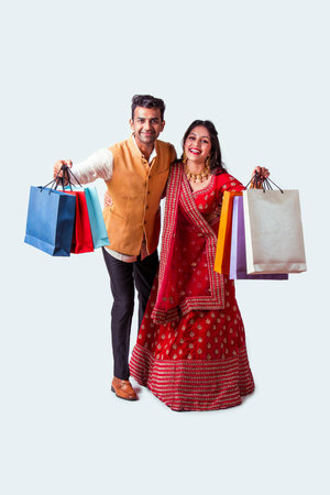 Indian asian couple with shopping bags in ethnic wear, standing isolated over white background. Diwali or festival saleの写真素材