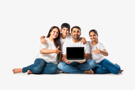 Indian asian young family of four using laptop computer while lying on floor or sitting isolated on whiteの写真素材