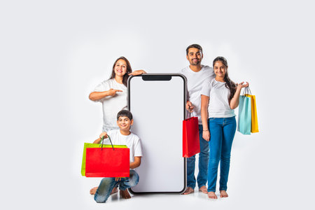 Indian asian family standing near tall smartphone holding shopping bags and pointing or promoting offerの写真素材