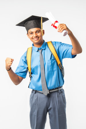 Indian Asian school boy in uniform and graduation cap, holding certificate roll, isolated and smilingの写真素材