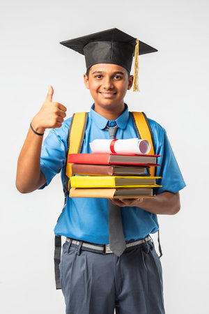 Indian Asian school boy in uniform and graduation cap, holding certificate roll, isolated and smilingの写真素材