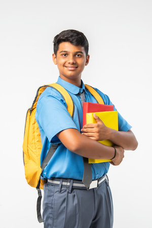Indian Asian school boy in uniform, holding books or laptop and backpack, isolated, smilingの写真素材