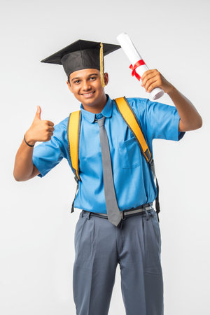 Indian Asian school boy in uniform and graduation cap, holding certificate roll, isolated and smilingの写真素材