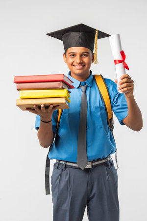 Indian Asian school boy in uniform and graduation cap, holding certificate roll, isolated and smilingの写真素材