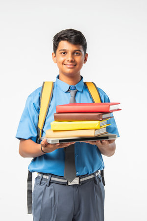 Indian Asian school boy in uniform, holding books or laptop and backpack, isolated, smilingの写真素材