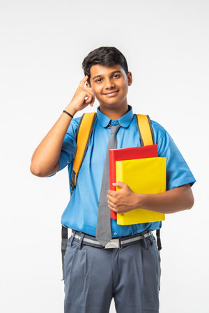Indian Asian school boy in uniform, holding books or laptop and backpack, isolated, smilingの写真素材