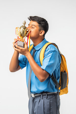 Indian Asian schoolboy in uniform holding a trophy and celebrating academic victory, isolated on...
