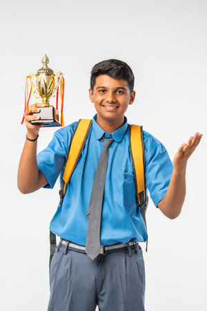 Indian Asian schoolboy in uniform holding a trophy and celebrating academic victory, isolated on whiteの写真素材