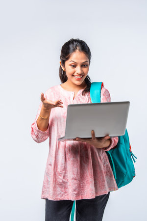 Indian asian young college girl with backpack, laptop, books pointing or ok signの写真素材