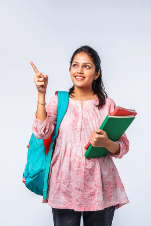 Indian asian young college girl with backpack, laptop, books pointing or ok sign