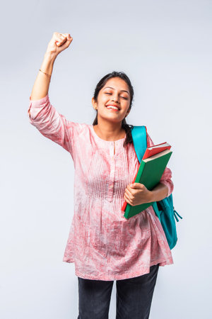 Indian asian young college girl with backpack, laptop, books pointing or ok signの写真素材