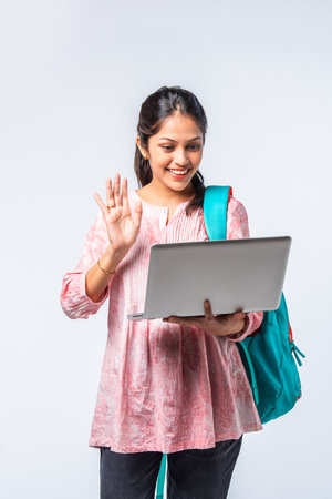 Indian asian young college girl with backpack, laptop, books pointing or ok signの写真素材