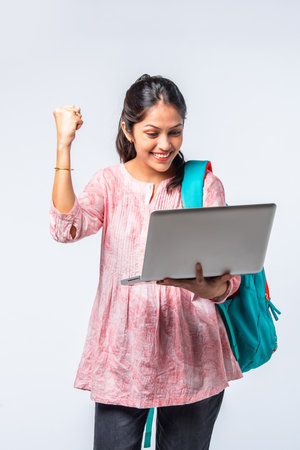 Indian asian young college girl with backpack, laptop, books pointing or ok signの写真素材