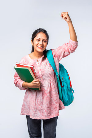 Indian asian young college girl with backpack, laptop, books pointing or ok signの写真素材